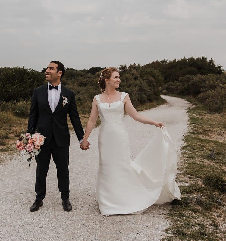 Bruidspaar hand in hand op een pad tussen de duinen